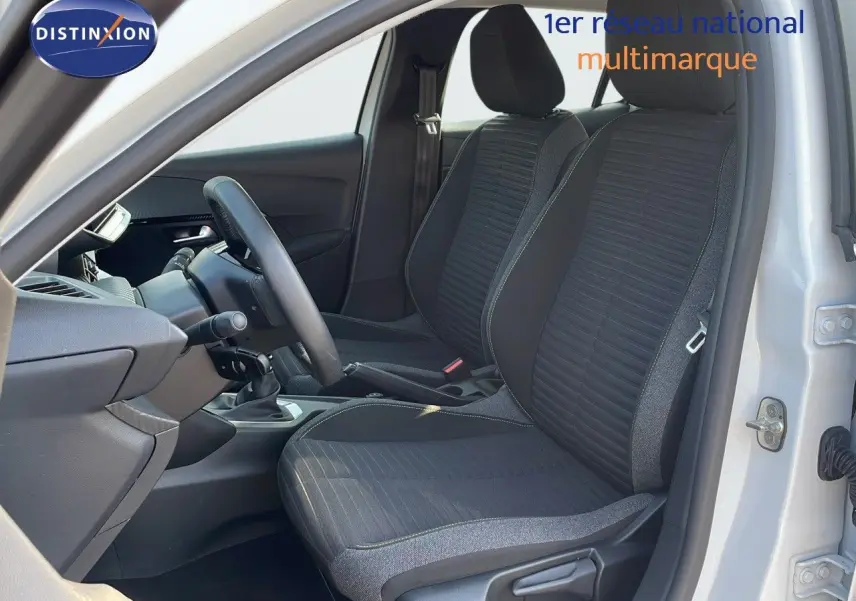 Vue intérieure côté conducteur de la Peugeot 208 blanche, montrant les sièges noirs et la console avec boîte manuelle.