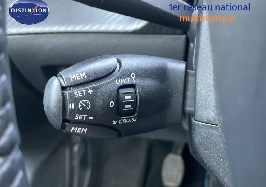 Gros plan sur la commande de régulateur de vitesse noire à gauche du volant dans un Peugeot 208 blanc banquise 2024.