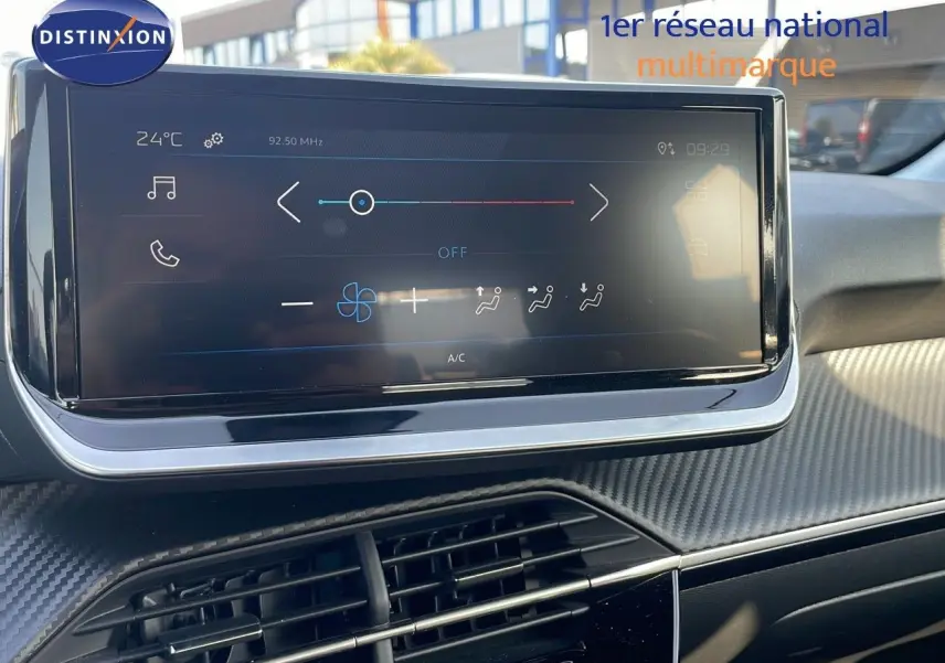Écran tactile central du tableau de bord de la Peugeot 208 2024, avec commandes climatisation et finition carbone.