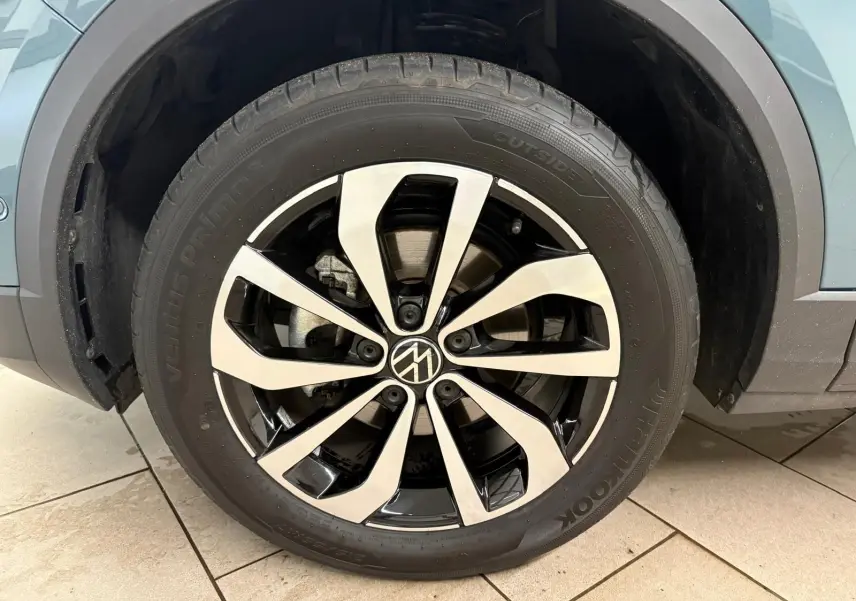 Gros plan sur la roue avant gauche du Volkswagen T-Roc bleu pétrole, mettant en valeur la jante alliage bicolore au design moderne.