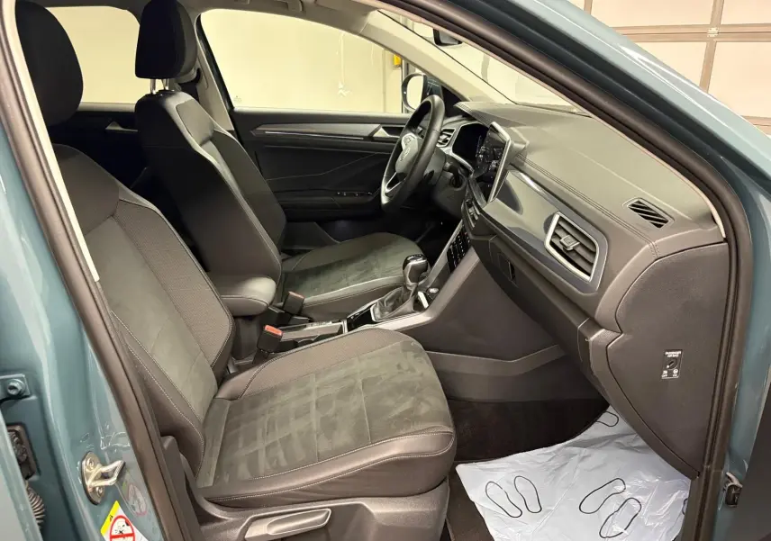 Vue intérieure côté conducteur du Volkswagen T-Roc 1.5 TSI bleu pétrole, mettant en valeur les sièges et le tableau de bord.