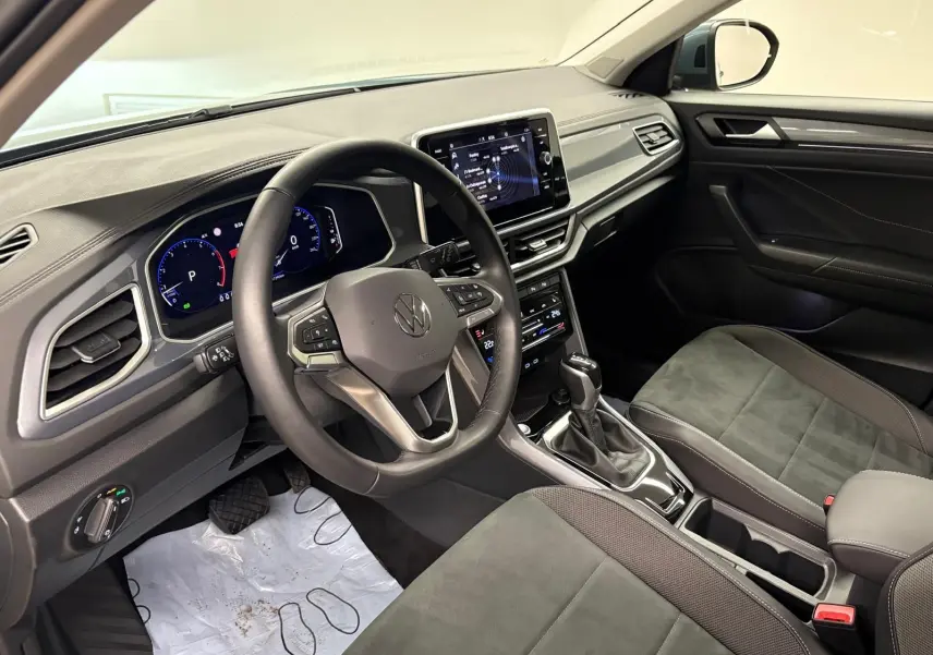 Vue intérieure côté conducteur du Volkswagen T-Roc 2025, volant multifonction, tableau de bord digital et sellerie noire.