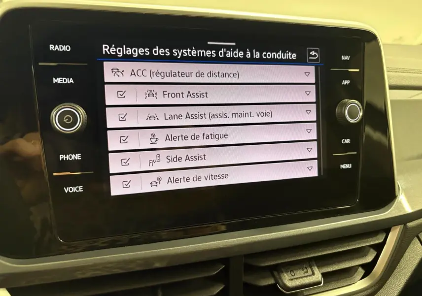 Écran tactile central du Volkswagen T-Roc 2025 affichant les réglages des aides à la conduite, avec commandes autour de l'écran.