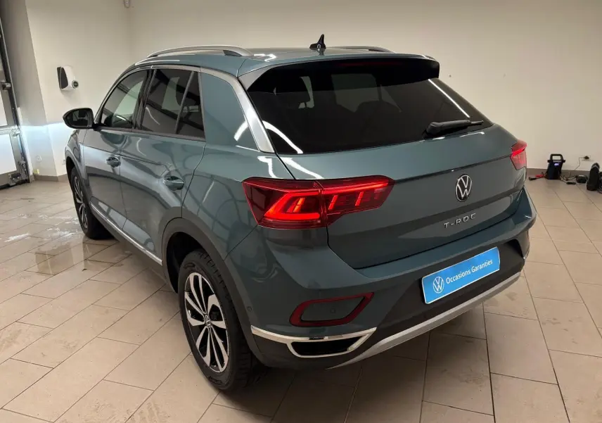 Vue 3/4 arrière droite d’un Volkswagen T-Roc 1.5 TSI 150 DSG7 Style Edition bleu pétrole avec feux arrière allumés en intérieur.