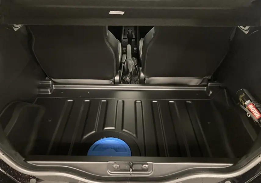 Coffre ouvert vu de l'arrière montrant un espace noir avec un réservoir bleu AdBlue et les sièges avant noirs du Ligier JS50.