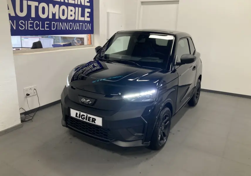 Vue 3/4 avant d'une Ligier JS50 noire 2026 avec feux LED allumés et jantes alu noires en intérieur showroom.