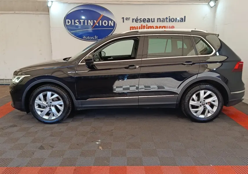 Vue de profil côté gauche d’un Volkswagen Tiguan noir 2022, avec jantes alliage et barres de toit chromées.
