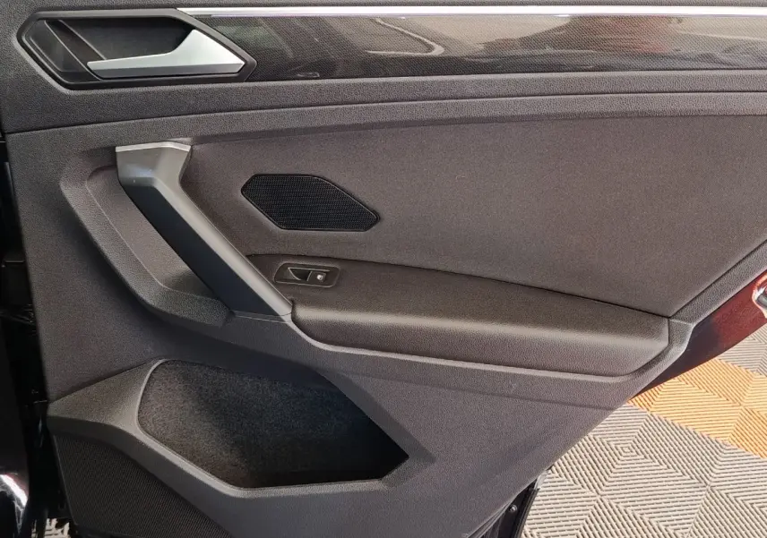Vue intérieure côté gauche de la porte arrière noire du Volkswagen Tiguan 2.0 TDI avec poignée et haut-parleur intégrés.