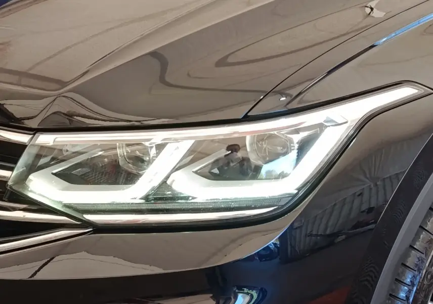 Gros plan sur le phare avant droit allumé du Volkswagen Tiguan noir 2022, soulignant ses LED distinctives.