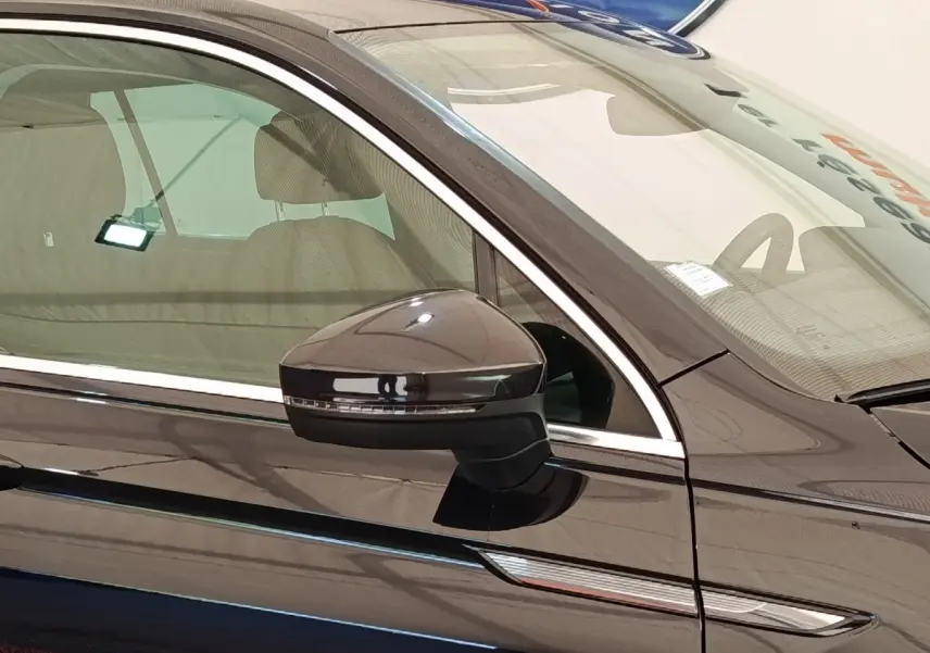 Gros plan sur le rétroviseur côté conducteur d’un Volkswagen Tiguan noir 2022 avec finition élégante et détails chromés.