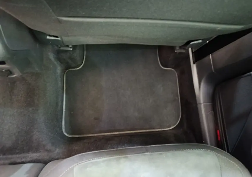 Vue intérieure du plancher côté passager avant d'un Volkswagen Tiguan noir, avec tapis de sol noir et siège partiellement visible.