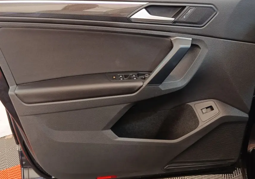 Vue intérieure côté gauche de la porte avant noire du Volkswagen Tiguan 2.0 TDI 150 DSG7 Elegance avec commandes électriques.