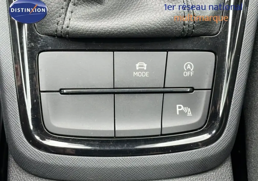 Gros plan sur les boutons de commande de mode de conduite et assistance au stationnement du Skoda Kamiq blanc glacier 2025.