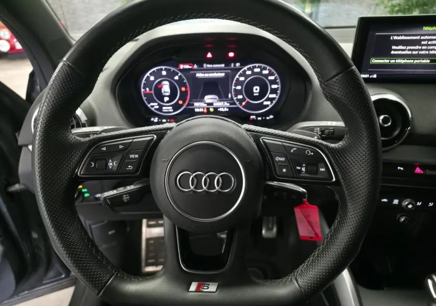 Vue rapprochée du volant sport S line en cuir noir avec méplat et tableau de bord numérique de l'Audi Q2 gris 2023.