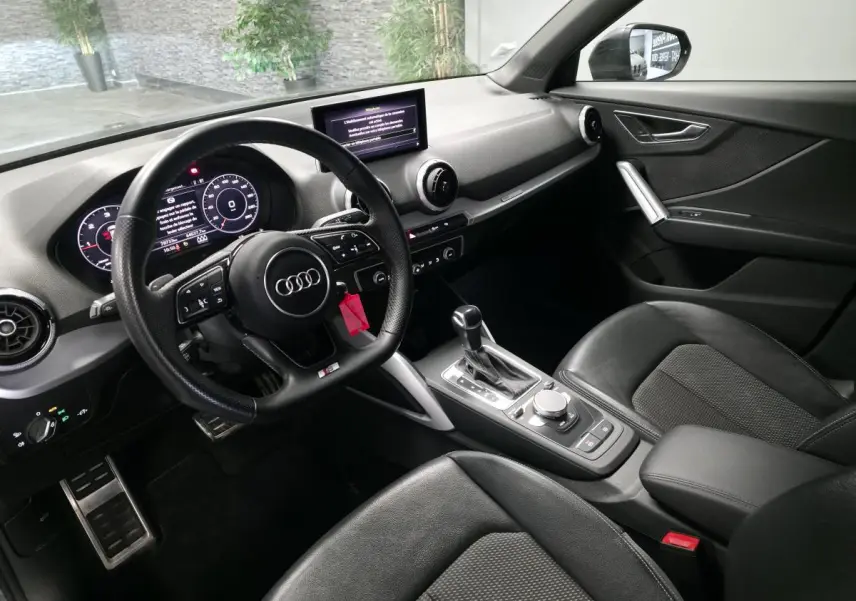 Vue intérieure côté conducteur de l'Audi Q2 S line Plus 2023, avec volant sport cuir noir et console centrale moderne.