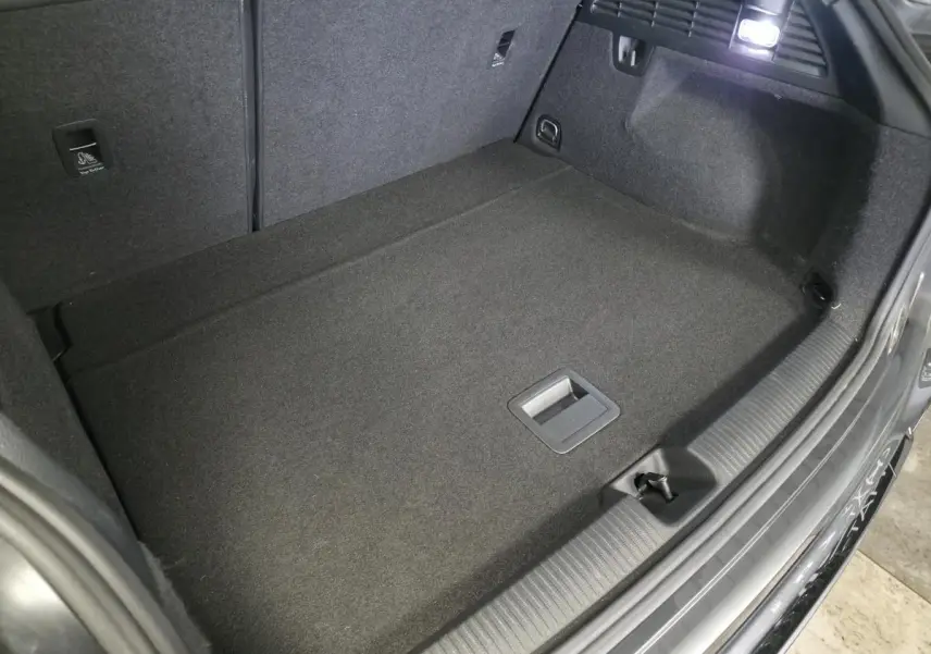 Vue intérieure du coffre spacieux et propre de l'Audi Q2 gris, avec éclairage et revêtement en tissu noir.