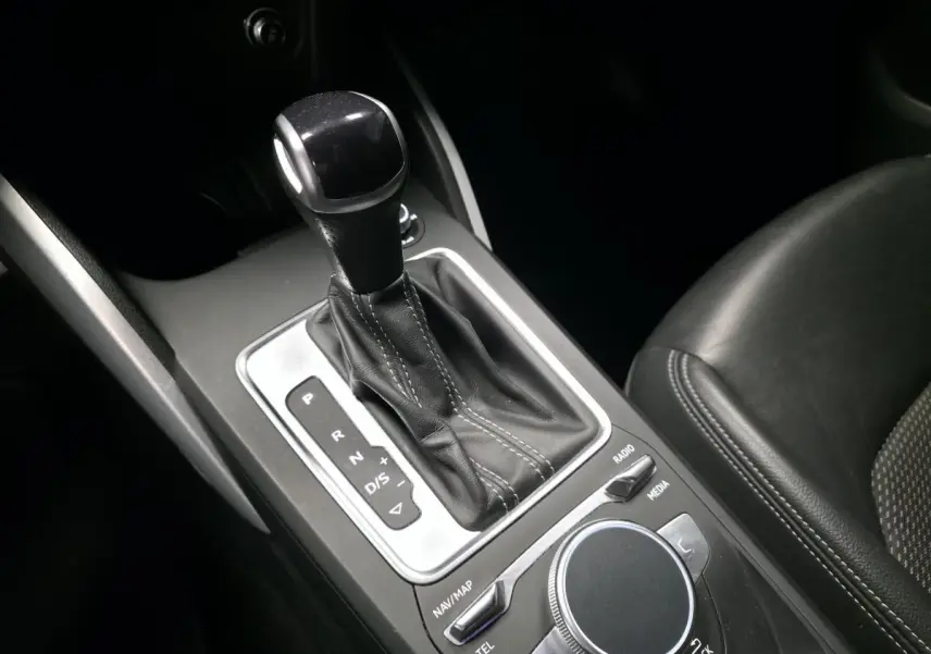 Gros plan sur la console centrale de l'Audi Q2 gris, montrant le levier de vitesse automatique et la molette de commande multimédia.