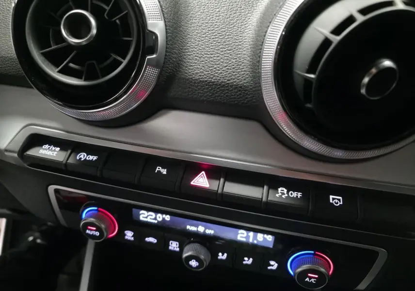Détail de la console centrale de l'Audi Q2 2023 gris, montrant les aérateurs ronds et les commandes de climatisation automatiques.