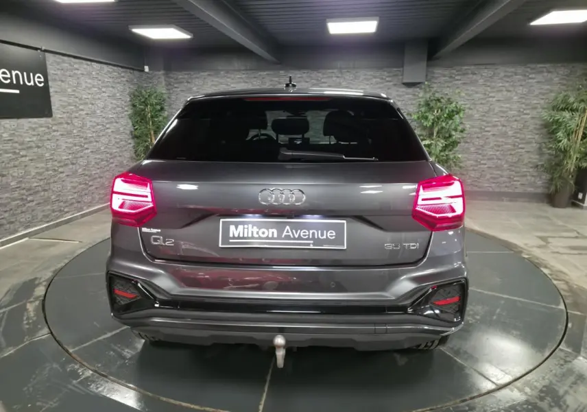 Vue arrière d’un Audi Q2 gris Daytona avec feux LED allumés et attelage amovible en intérieur showroom.