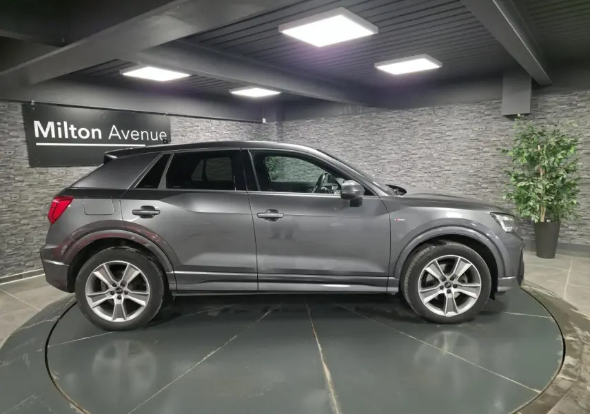 Audi Q2 gris Daytona en vue profil côté gauche, avec jantes alliage 18 pouces et badge S line visible.