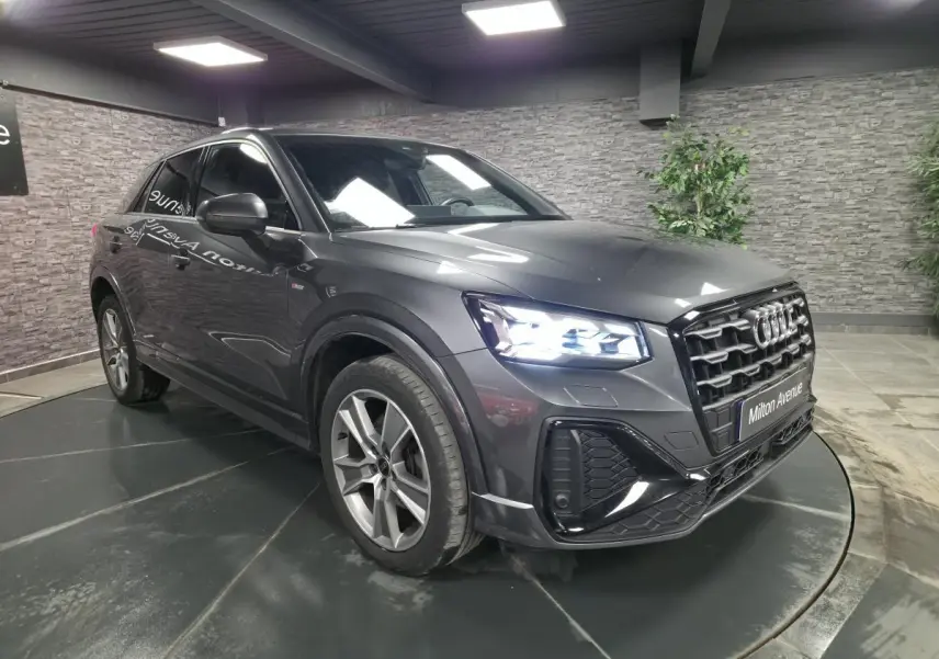 Audi Q2 gris Daytona en 3/4 avant droit avec phares Matrix LED allumés dans un showroom intérieur.