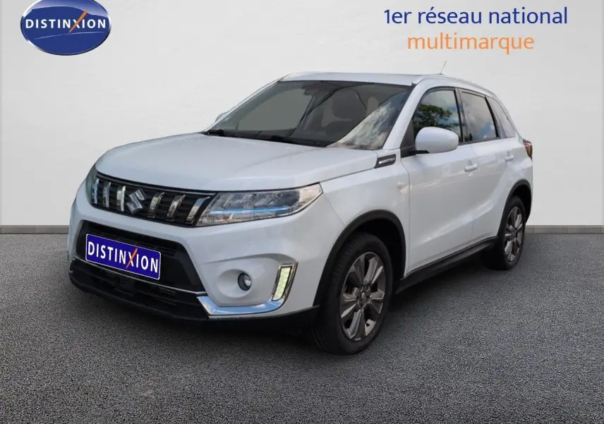 Suzuki Vitara blanc vue 3/4 avant droit, calandre chromée et jantes alliage visibles sur fond neutre.