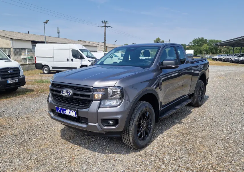 Ford Ranger Super Cabine gris carbone en 3/4 avant droit, avec marchepied noir et jantes noires sur terrain gravelé.