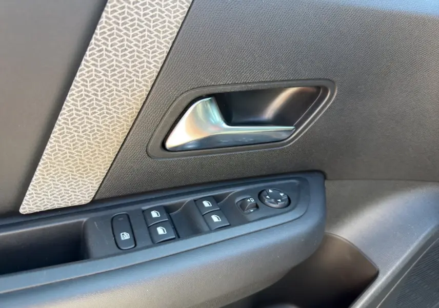 Gros plan sur la poignée intérieure et les commandes de vitres côté conducteur d'une Citroën C4 2023, tissu gris et plastique noir.