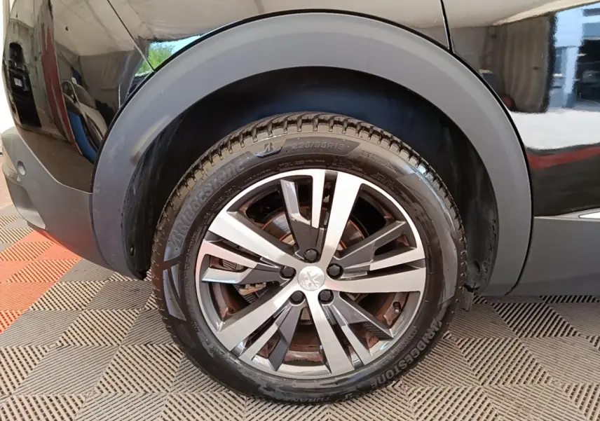 Gros plan sur la roue avant droite d’un Peugeot 3008 noir, mettant en valeur la jante alliage et le pneu Bridgestone.