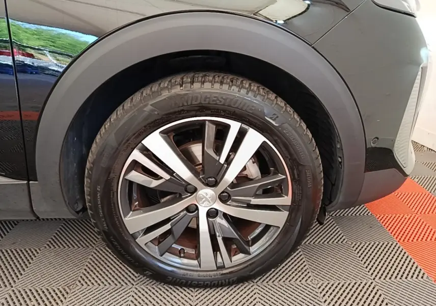 Gros plan sur la roue avant gauche noire du Peugeot 3008 avec jante alliage bicolore et pneu Bridgestone.