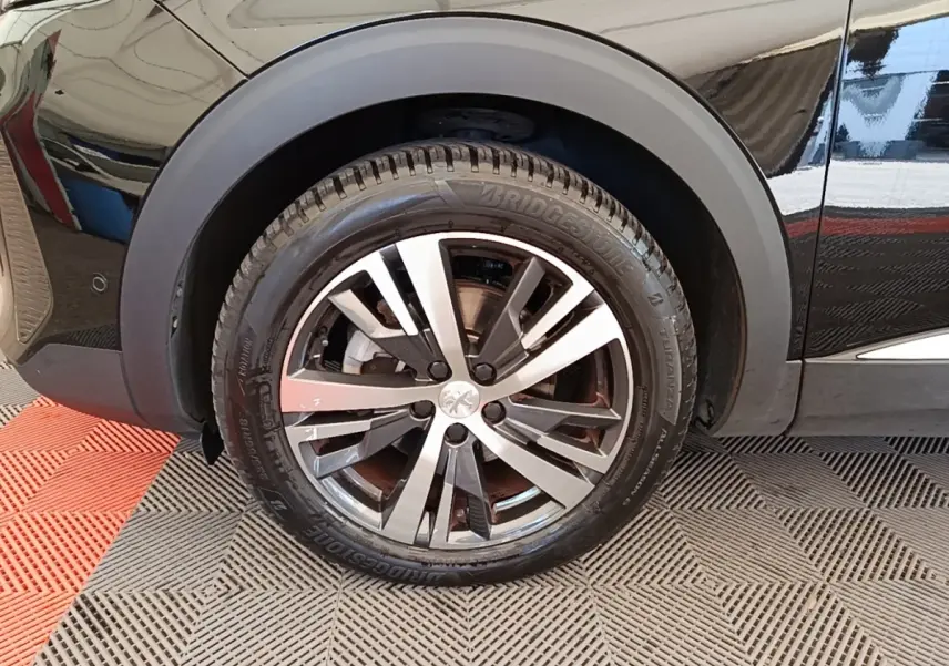 Gros plan sur la roue avant gauche noire du Peugeot 3008 PureTech 130 Allure, jante alliage bicolore.