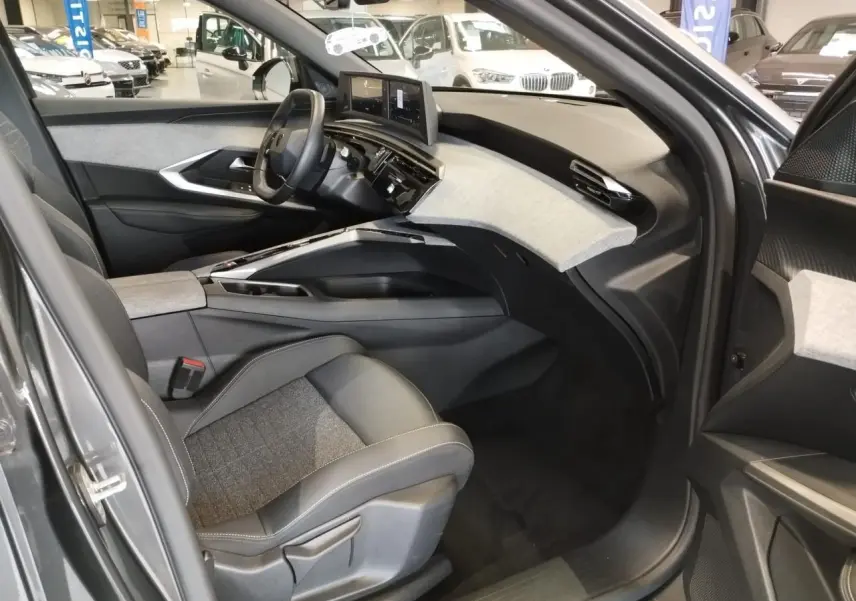 Vue intérieure côté conducteur du Peugeot 5008 2025 gris titanium, avec tableau de bord moderne et sellerie tissu gris et cuir noir.