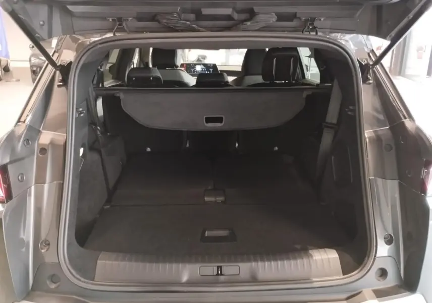 Coffre ouvert vu de l'arrière d'un Peugeot 5008 gris titanium avec banquette arrière rabattue et cache-bagages déployé.