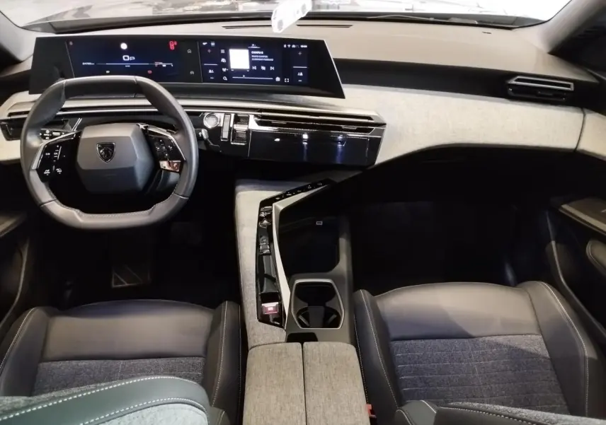 Vue intérieure avant du Peugeot 5008 2025, tableau de bord moderne avec double écran et sellerie tissu gris et cuir noir.