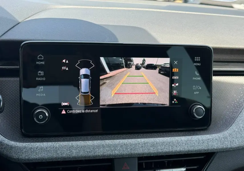 Écran tactile intérieur du Skoda Kamiq 2025 montrant la caméra de recul avec alertes de distance, tableau de bord gris.