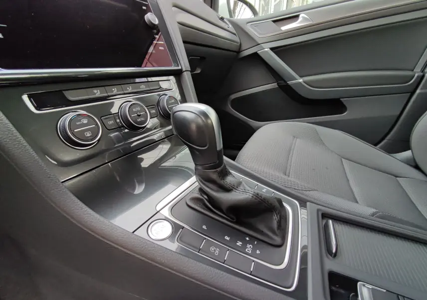 Gros plan sur la console centrale et levier de vitesse automatique d’une Volkswagen Golf blanche, intérieur gris.