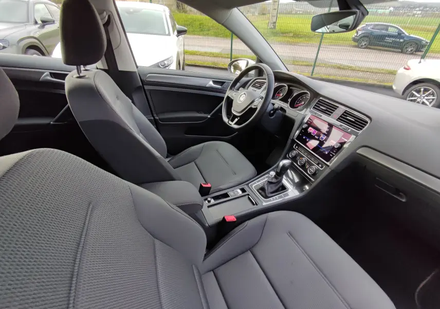 Vue intérieure côté conducteur de la Volkswagen Golf blanche 2019, montrant le tableau de bord et la console centrale moderne.