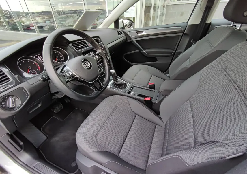 Vue intérieure côté conducteur de la Volkswagen Golf blanche 1.5 TSI Evo 2019, avec tableau de bord et sièges gris.