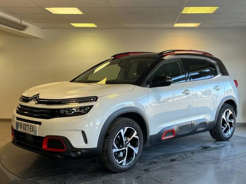 Vue 3/4 avant droite d'un Citroën C5 Aircross blanc nacré avec toit noir et accents rouges sur les bas de caisse et calandre.