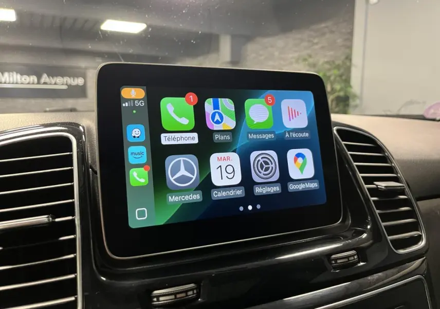 Écran tactile central du Mercedes GLE 2018 affichant Apple CarPlay avec icônes colorées, entouré de grilles d'aération noires.