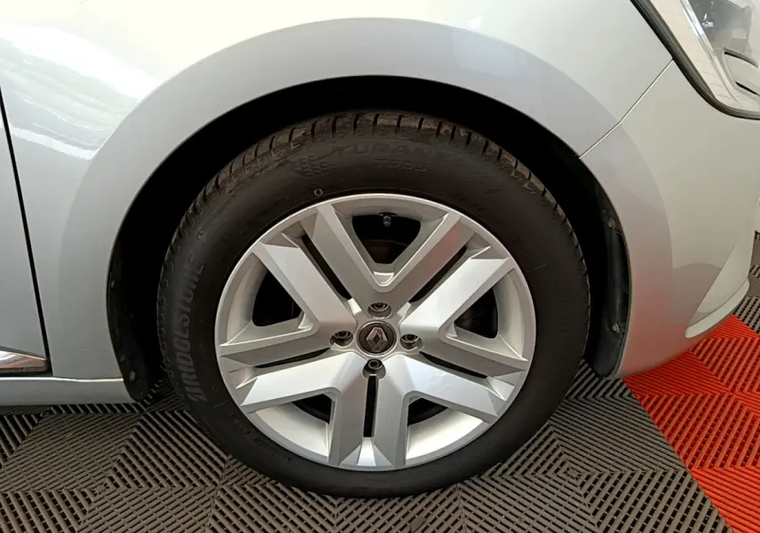 Gros plan sur la roue avant droite d'une Renault Clio gris clair, mettant en valeur la jante alliage et le logo central.