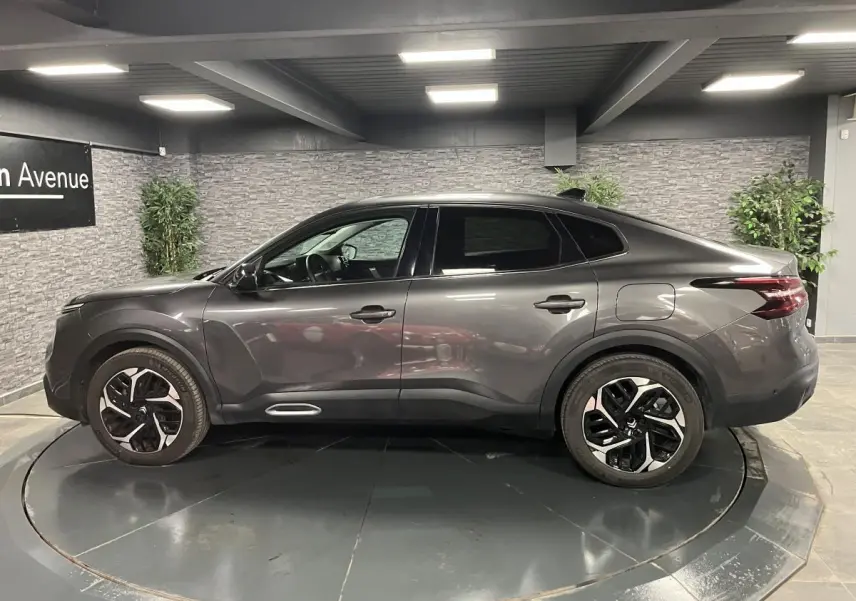 Profil côté gauche d'une Citroën C4 X gris métallisé 2024 avec jantes alliage 18'' Aeroblade en intérieur showroom.