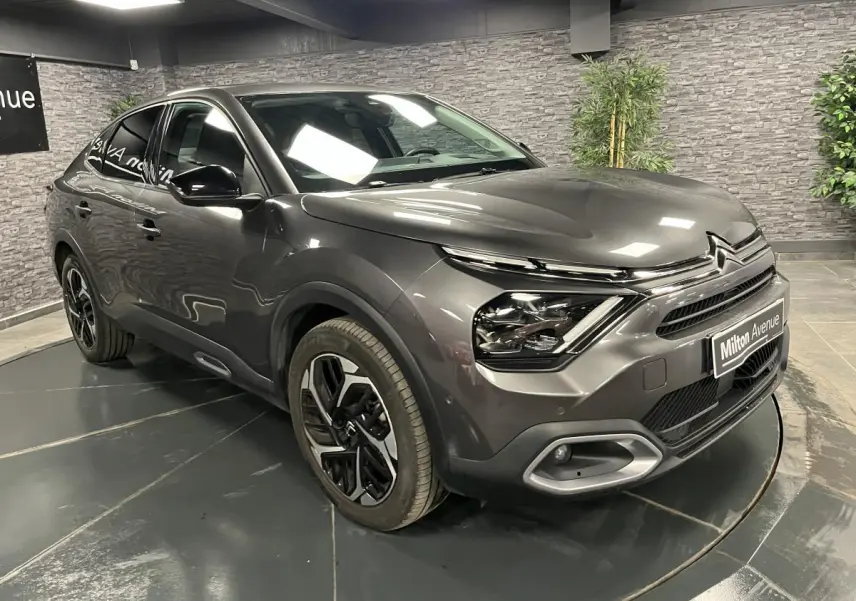 Citroën C4 X gris métallisé vue 3/4 avant droit avec jantes alliage et projecteurs LED en intérieur showroom.