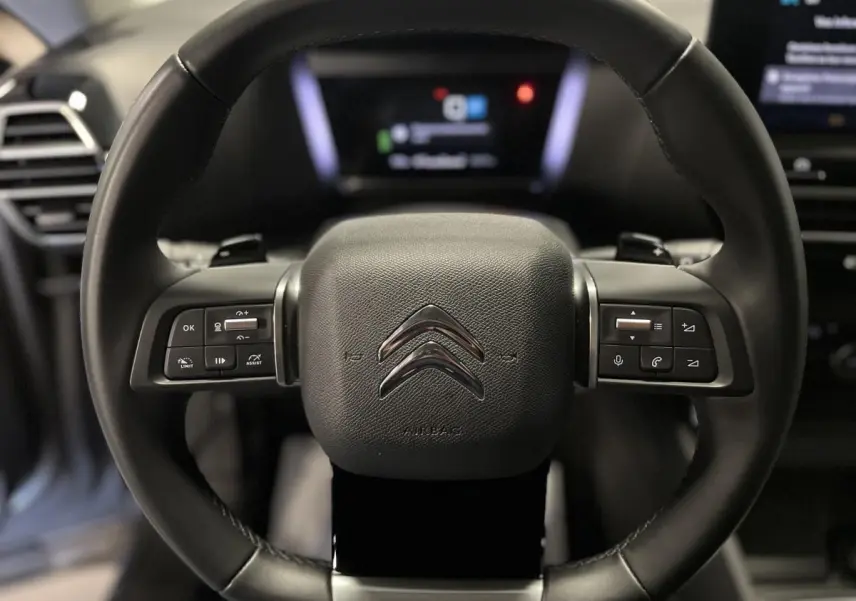 Gros plan sur le volant cuir noir de la Citroën C4 X 2024 avec commandes intégrées et logo chromé central.