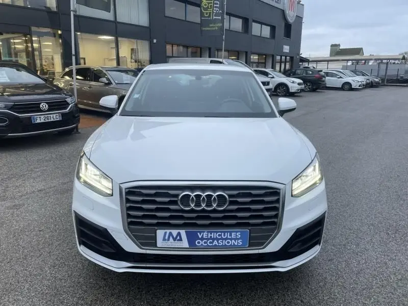 Vue de face d'un Audi Q2 blanc 30 TFSI 116 SPORT LIMITED de 2020 avec phares allumés et calandre noire hexagonale.