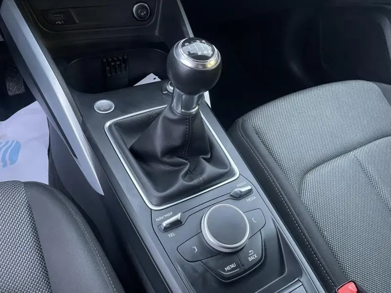 Vue rapprochée de la console centrale de l’Audi Q2 blanche 30 TFSI 116 SPORT LIMITED avec levier de vitesse manuel et commandes multimédia.