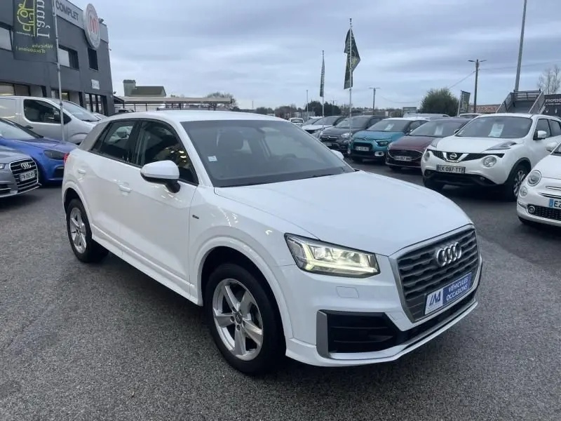 Audi Q2 blanc vue 3/4 avant droit, phares allumés, calandre noire et jantes alliage cinq branches.
