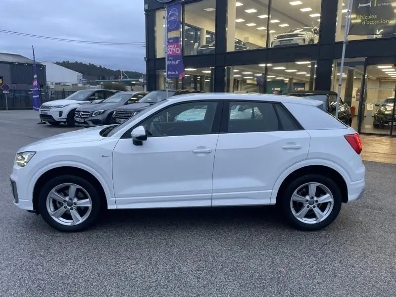 Audi Q2 blanc en vue de profil côté gauche, version 30 TFSI 116 SPORT LIMITED, stationné devant un showroom.