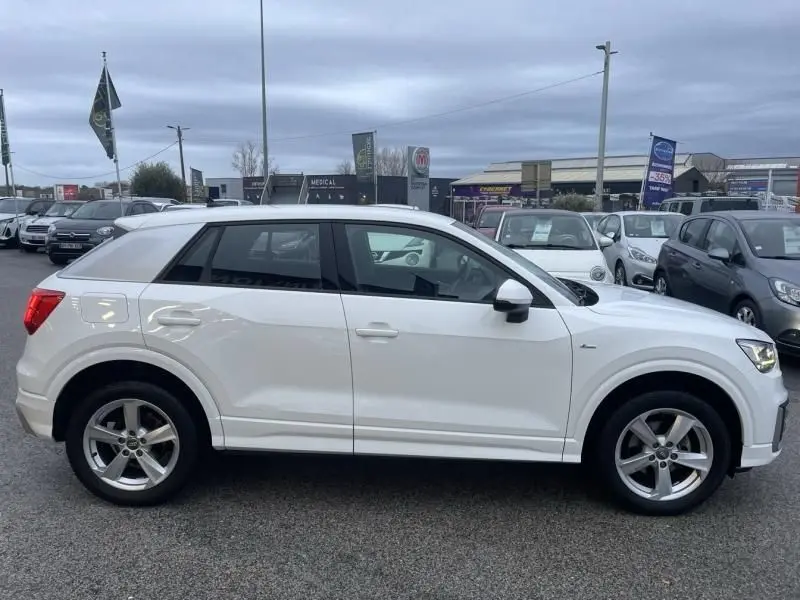 Vue de profil côté gauche d'un Audi Q2 blanc 30 TFSI 116 SPORT LIMITED de 2020 sur un parking extérieur.