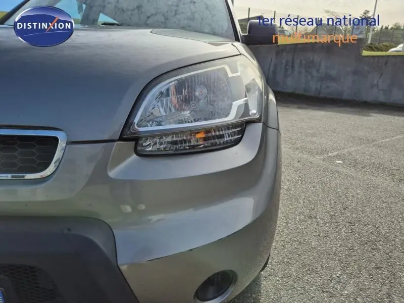 Gros plan sur l'avant droit d'une KIA SOUL 2010 gris métallisé, mettant en valeur le phare et la calandre.